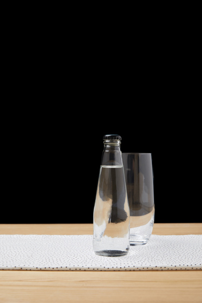 Botella con agua y vaso vacío sobre mesa sobre fondo negro
 - Foto, Imagen
