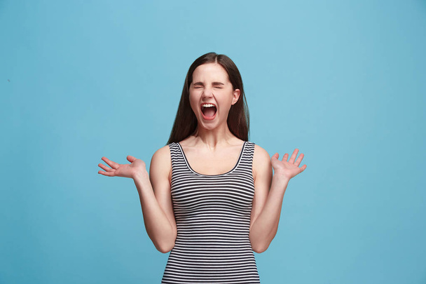 The young emotional angry woman screaming on blue studio background - Fotó, kép