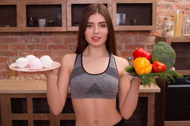 Jíst více zeleniny! Mladá atraktivní fitness dívka s nahý trup nabízejí lidem jako protiváhu z jedné ruky zeleninu a jiné sladkosti. - Fotografie, Obrázek