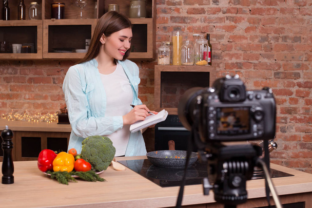 Jeść zdrowo jest naprawdę bogaty! Atrakcyjne, uśmiechając się przystojny vlogger piśmie przepis na jej blogu wideo w celu gotować warzywa dla siebie i jednoczącej ludzi, jeść zdrową żywność. - Zdjęcie, obraz