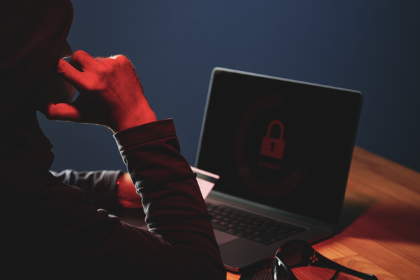 Visão traseira do criminoso cibernético roubando detalhes do cartão de crédito e hackear laptop no escuro
 - Foto, Imagem