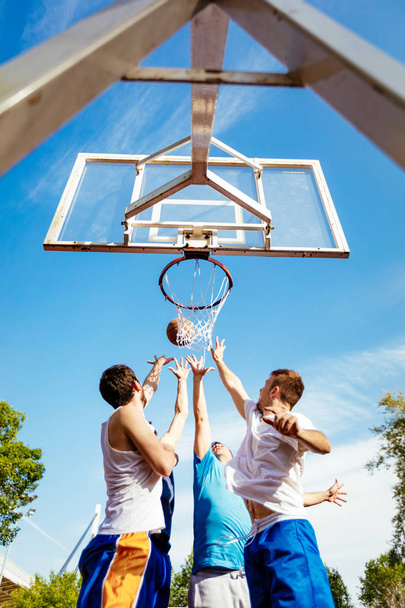 Four basketball players have a training outdoor. They are playing and jumping for alley oop. - Foto, Imagen