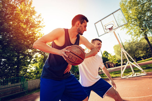 Два вуличні баскетболісти грають один на одному. Вони роблять добрі дії і охороняють м'яч
. - Фото, зображення