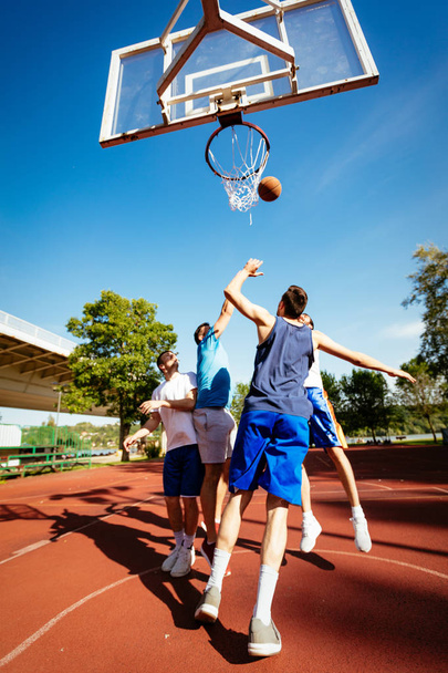 Čtyři basketbalisté mají venkovní trénink. Hrají si a skákání pro alley oop. - Fotografie, Obrázek