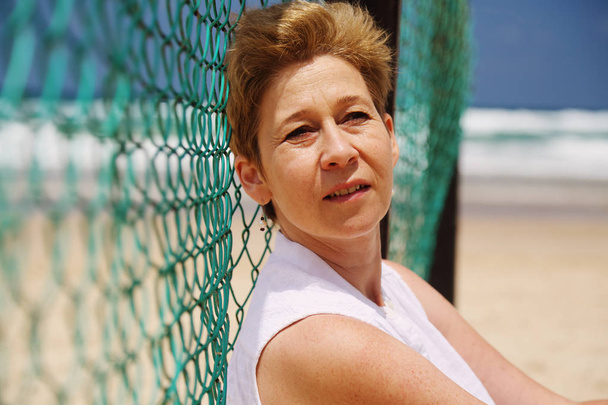 kypsä nainen istuu meren rannalla
 - Valokuva, kuva