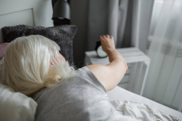 Senior woman lying in bed turning off alarm clock - Фото, зображення