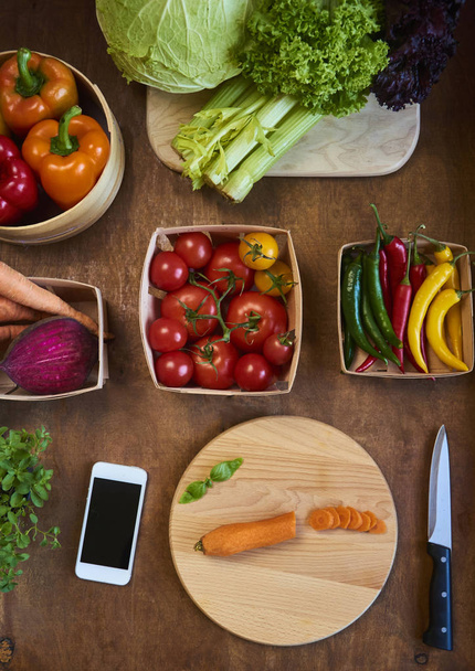 Нарезанная морковь на деревенской разделочной доске кухонным ножом и смартфоном. Ингредиенты для вкусной вегетарианской кухни
 - Фото, изображение