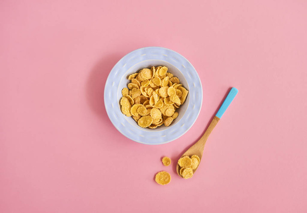 Placa azul de cereales y cuchara sobre fondo rosa, vista superior
 - Foto, Imagen