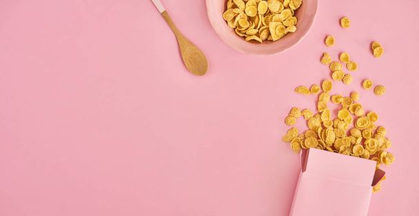 Box of cereals, pink plate and spoon on pink background, top view. Design mockup with space to input your text - Φωτογραφία, εικόνα