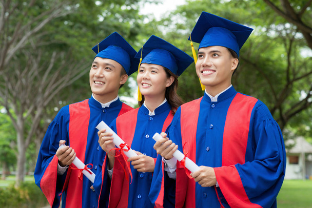 Graduados vietnamitas confiados con diplomas en las manos de pie en fila y mirando hacia el futuro con optimismo, retrato en la cintura
 - Foto, imagen