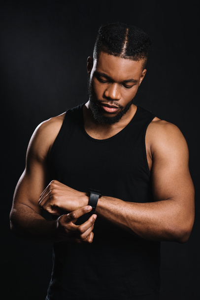 knappe ernstige Afro-Amerikaanse sportman met smartwatch geïsoleerd op zwart - Foto, afbeelding