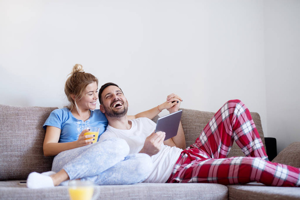 glückliches junges Liebespaar, das auf dem Sofa sitzt und gemeinsam Filme anschaut und Tablet-PC benutzt - Foto, Bild