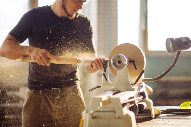 man working at small wood lathe, an artisan carves piece of wood - Foto, afbeelding