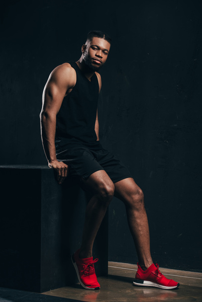 full length view of handsome young african american sportsman sitting and looking at camera  - Photo, Image