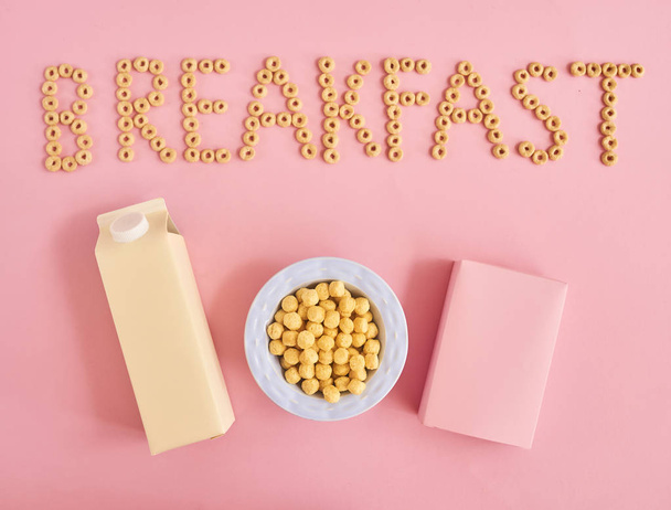 Plate of cereals or cornflakes, bottle of milk, box and word Breakfast on pink background, top view - Foto, Bild
