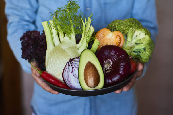 Primer plano de manos masculinas sosteniendo plato grande con diferentes verduras frescas de granja. Cosecha otoñal y alimentos orgánicos saludables
 - Foto, Imagen