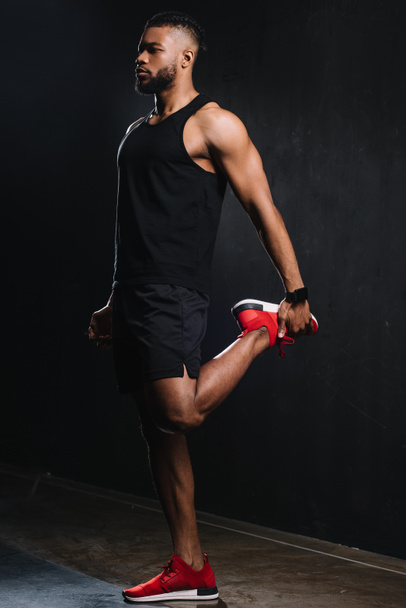 full length view of young african american sportsman stretching muscles on black  - Foto, immagini