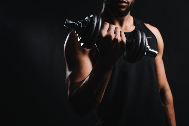 cropped shot of muscular african american man exercising with dumbbell isolated on black  - 写真・画像