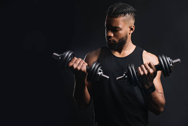 handsome muscular african american man exercising with dumbbells isolated on black - Photo, Image