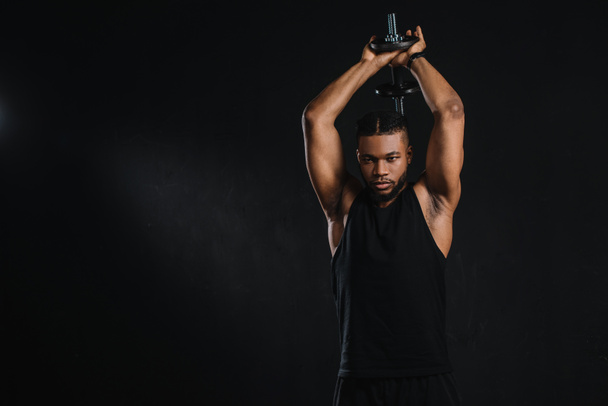 athletic young african american man exercising with dumbbell isolated on black  - Foto, Bild