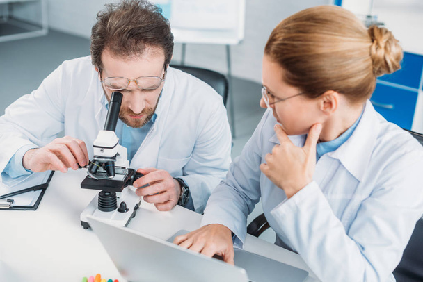 портрет научных сотрудников в белых халатах, работающих вместе на рабочем месте с микроскопом в лаборатории
 - Фото, изображение