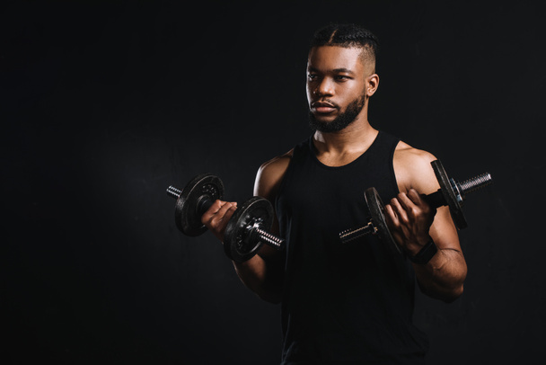молодой африканский американский спортсмен, тренирующийся с гантелями и смотрящий в сторону, изолированный от черного
 - Фото, изображение
