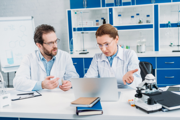 retrato de científicos en batas de laboratorio y anteojos trabajando juntos en el lugar de trabajo con portátil en el laboratorio
 - Foto, Imagen