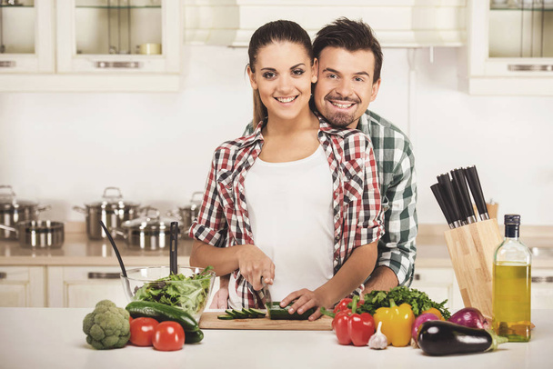Beautiful young couple in the kitchen while cooking. Looking at the camera - Fotoğraf, Görsel