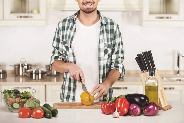 Homem está cozinhando salada de legumes na cozinha
 - Foto, Imagem