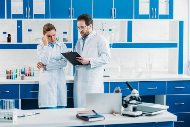 научные исследователи в белых халатах и очках с блокнотом в лаборатории
 - Фото, изображение