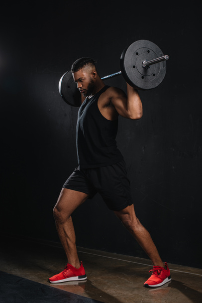 muscular young african american sportsman lifting barbell on black  - 写真・画像
