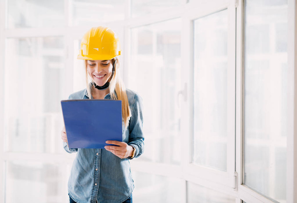 young happy female engineer with yellow helmet looking at blueprint - Photo, Image
