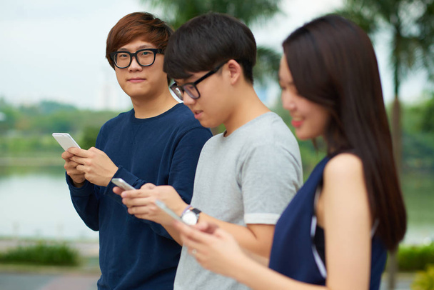 Koreański nastolatków za pomocą aplikacji na smartfony, stojąc na zewnątrz - Zdjęcie, obraz