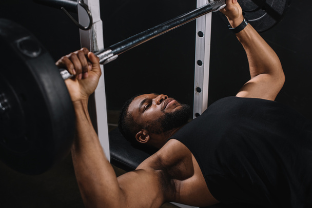 スポーツウェアのバーベルを持ち上げる筋肉の若いアフリカ系アメリカ人男性 - 写真・画像