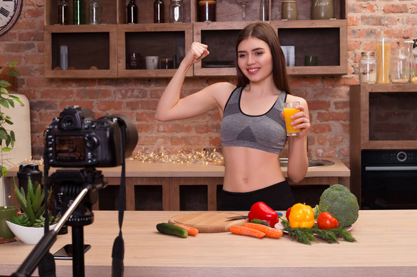 Comprometa-se a estar em forma! Menina atraente jovem enquanto está na cozinha e bebendo um suco de laranja, mostrando seu corpo forte e apto para todos para a câmera
. - Foto, Imagem
