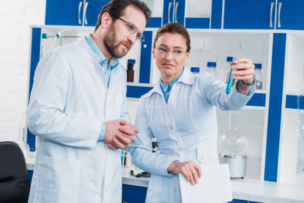retrato de científicos en anteojos mirando tubo con reactivo en laboratorio
 - Foto, imagen