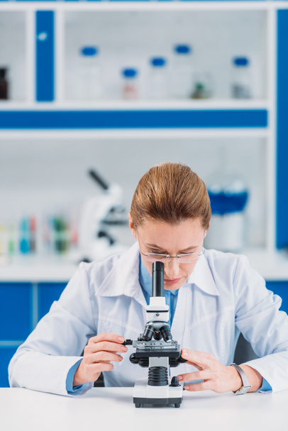 female scientist in eyeglasses looking on reagent through microscope in laboratory - Zdjęcie, obraz