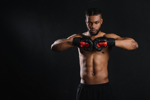 muscular shirtless african american boxer in boxing gloves looking at camera isolated on black  - Fotoğraf, Görsel