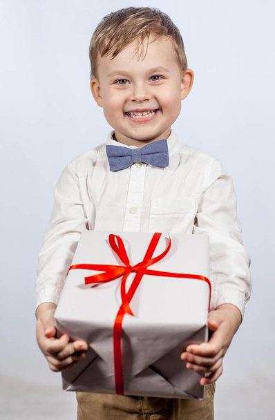 Cute little boy with a gift. Happy boy holding a box with a gift. Mothers Day. International Women's Day. Portrait of a happy little boy on a white background. Spring. Birthday. - Фото, зображення