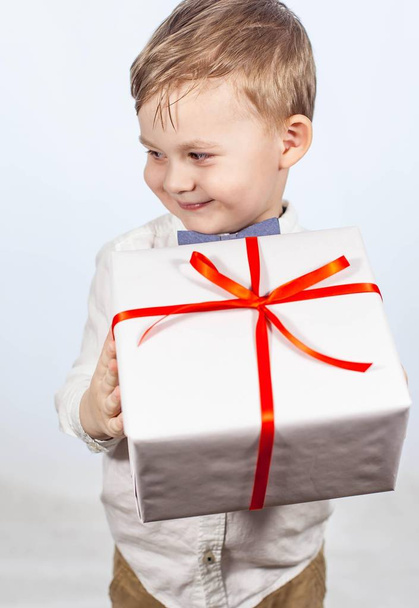Cute little boy with a gift. Happy boy holding a box with a gift. Mothers Day. International Women's Day. Portrait of a happy little boy on a white background. Spring. Birthday. - Foto, imagen
