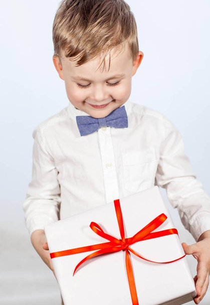 Cute little boy with a gift. Happy boy holding a box with a gift. Mothers Day. International Women's Day. Portrait of a happy little boy on a white background. Spring. Birthday. - Foto, imagen