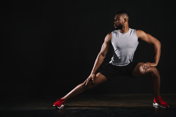athletic young african american man in sportswear exercising and looking away on black - Foto, afbeelding