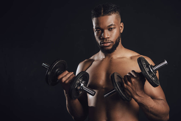 muscolare senza maglietta africano americano sportivo formazione con manubri e guardando la fotocamera isolata su nero
  - Foto, immagini