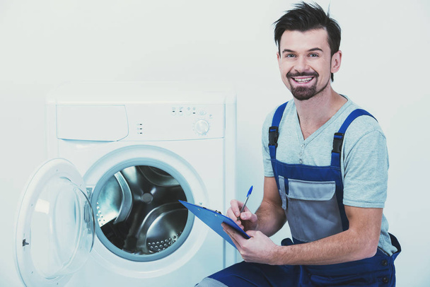 Repairman is repairing a washing machine on the white background - Foto, afbeelding