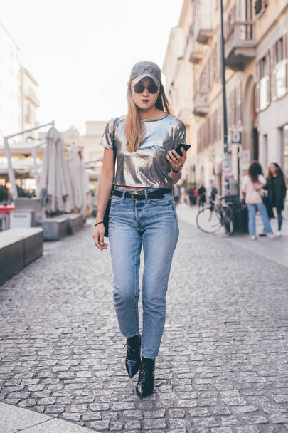 young woman outdoors walking looking away holding smart phone - traveller, influencer, blogger concept - Photo, Image