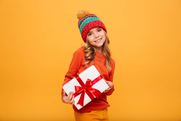 Pleased Young girl in sweater and hat holding gift box - Φωτογραφία, εικόνα