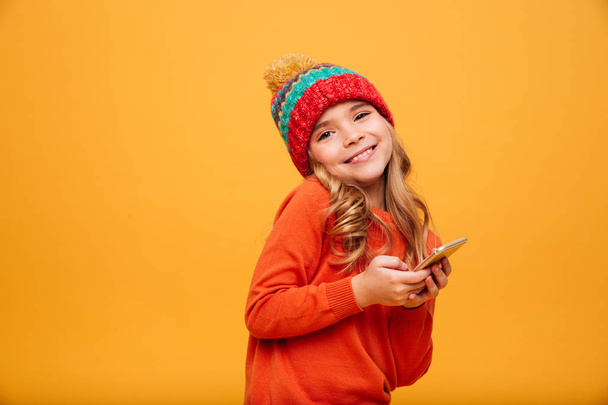Smiling Young girl in sweater and hat holding smartphone - Valokuva, kuva