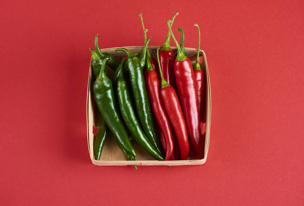 Modello decorativo di peperoncino caldo con code verdi in scatola su sfondo rosso, vista dall'alto
 - Foto, immagini