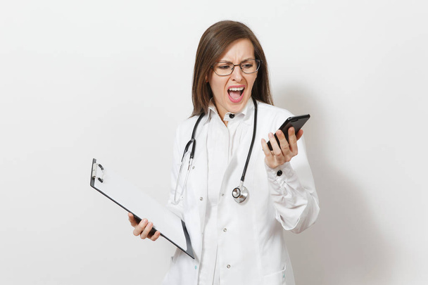 Ενδιαφερόμενο γιατρό σοκαρισμένος γυναίκα με στηθοσκόπιο, απομονώνονται σε λευκό φόντο. Γυναίκα γιατρό σε ιατρική φόρεμα μιλούν στο κινητό τηλέφωνο, κατέχουν κάρτα υγείας στο Σημειωματάριο (Notepad) φάκελο. Έννοια του προσωπικού υγειονομικής περίθαλψης. - Φωτογραφία, εικόνα