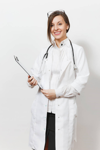 Smiling confident young doctor woman with stethoscope, glasses isolated on white background. Female doctor in medical gown holding health card on notepad folder. Healthcare personnel medicine concept. - Foto, imagen
